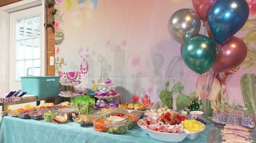 A colorful party table with snacks, fruits, and balloons against a vibrant, festive backdrop.
