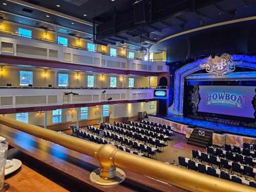 Interior of a theater with rows of tables set for an event, a stage with "SHOWBOAT" sign, and large windows.