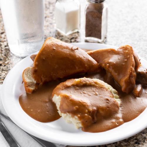 A plate of bread and biscuits smothered in brown gravy, with salt and pepper shakers and a glass of water in the background.