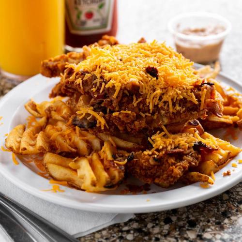 A plate of crispy fried chicken topped with melted cheese, served over waffle fries with ketchup and dipping sauce on the side.