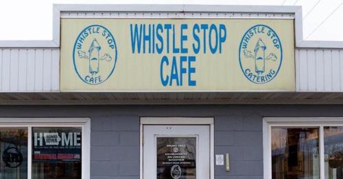 Sign for Whistle Stop Cafe featuring blue text and a graphic of a train whistle on a light background.