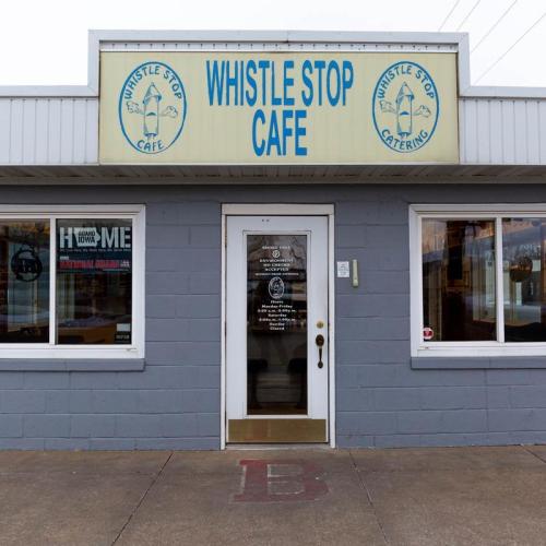 Exterior of Whistle Stop Cafe, featuring a sign and a welcoming entrance with a gray facade.