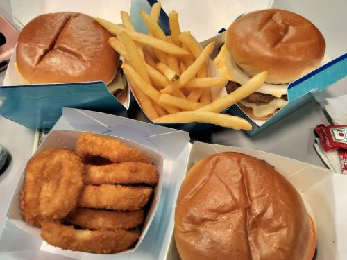 Four burgers, a serving of fries, and a box of onion rings arranged on a table.