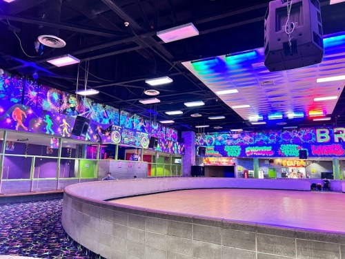 A brightly lit indoor roller skating rink with colorful neon decorations and a smooth wooden floor.