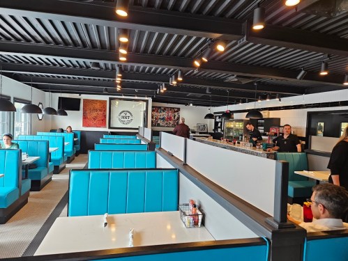 A modern restaurant interior featuring blue booths, a bar area, and staff serving customers.