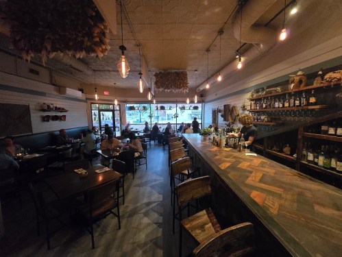 A cozy restaurant interior with wooden decor, a bar, and diners enjoying their meals in a warm atmosphere.