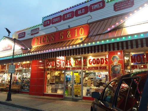 A brightly lit storefront of "Dick's 5 & 10" featuring colorful signage and a variety of goods displayed in the windows.
