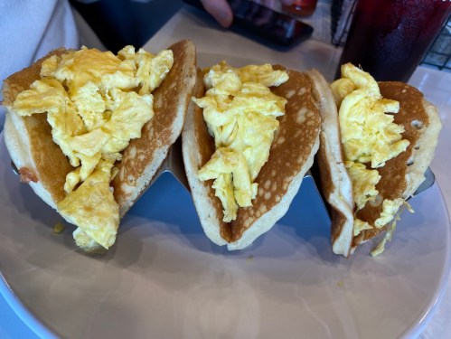 Three fluffy pancakes filled with scrambled eggs, served on a white plate. A drink is partially visible in the background.