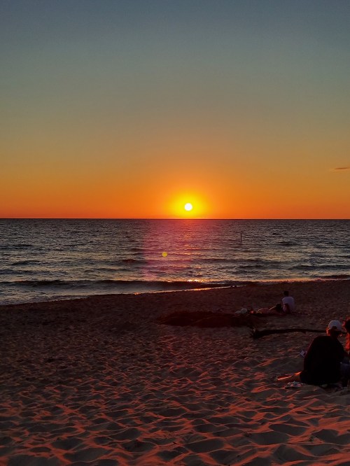 A serene beach at sunset, with vibrant orange and yellow hues reflecting on the calm ocean waves.