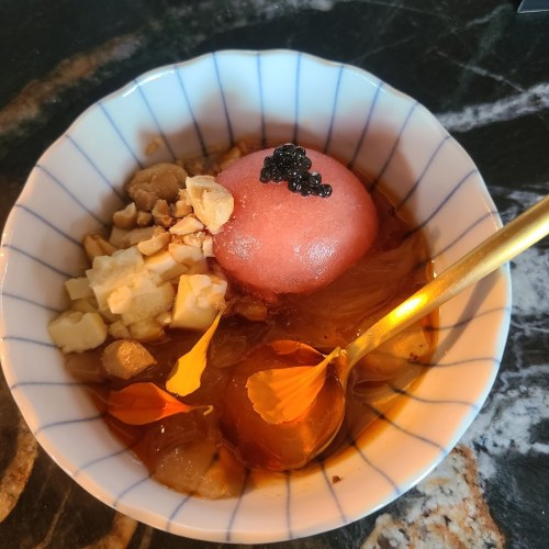 A bowl of dessert featuring a pink sorbet, nuts, and caviar, served in a decorative dish with a golden spoon.
