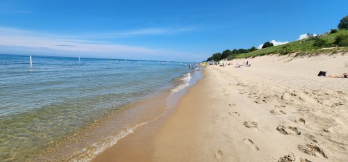 A sandy beach with gentle waves, clear blue sky, and people enjoying the sun along the shoreline.