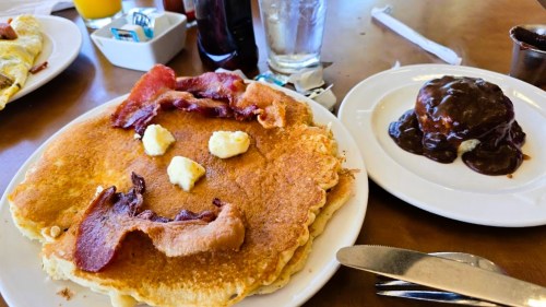 A large pancake topped with bacon and butter, alongside a chocolate dessert on a plate.