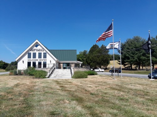 A welcome center in West Virginia with flags and a clear blue sky, surrounded by green grass and trees.