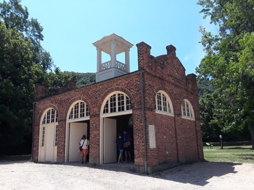 A brick building with arched windows and a cupola, surrounded by trees and people exploring the area.