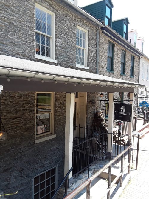 A stone building with a porch and a sign reading "Stone House," surrounded by other historic structures.