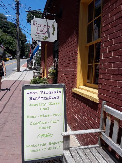 A sign outside a shop reads "West Virginia Handcrafted" with items like jewelry, candles, and postcards listed.