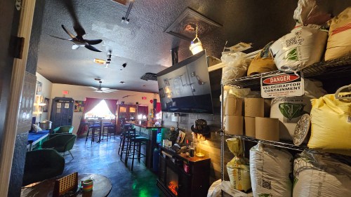 A cozy interior of a café with shelves of supplies, a bar area, and a TV, featuring playful decor and a welcoming atmosphere.
