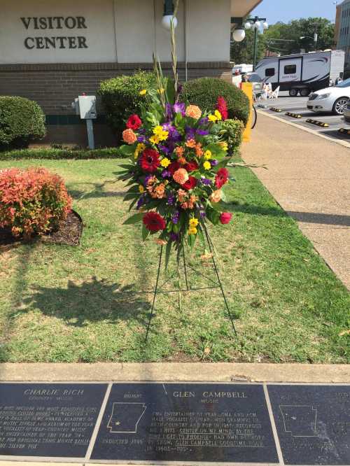 A colorful floral arrangement stands near a plaque honoring Glen Campbell and Charlie Rich outside a visitor center.