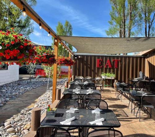 Outdoor dining area with black tables, hanging flower baskets, and a large "EAT" sign under a shaded canopy.