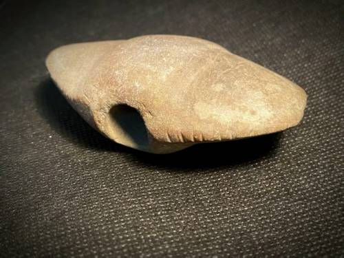 A smooth, oval-shaped stone with a hollowed section, resting on a dark textured surface.