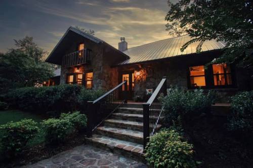 A cozy stone house at dusk, featuring a front staircase and warm lights glowing from the windows.