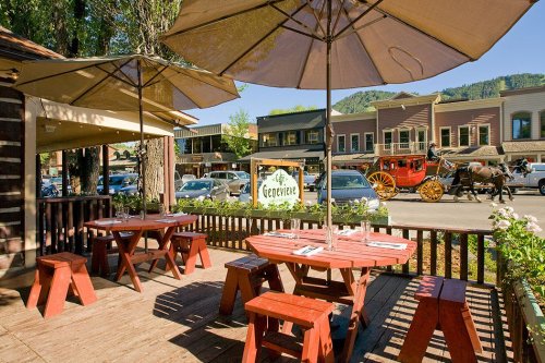 Outdoor dining area with red picnic tables and umbrellas, overlooking a street with a horse-drawn carriage and shops.