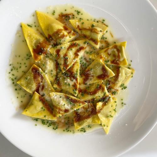 A plate of yellow ravioli drizzled with sauce and sprinkled with chives and grated cheese.