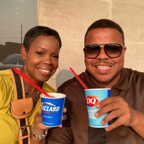 A smiling couple holds ice cream cups outside, enjoying a sunny day together.