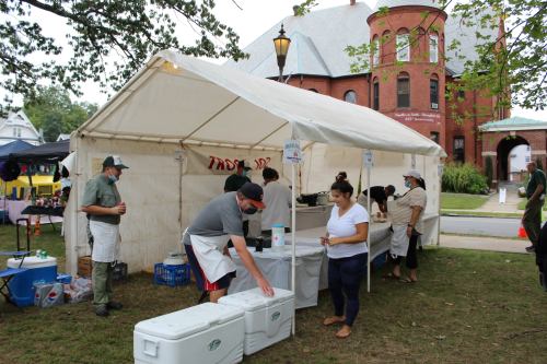 A group of people working at a food tent, preparing and serving items outdoors at a community event.