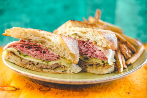 A close-up of a sandwich filled with layers of meat and cheese, served with a side of fries on a plate.