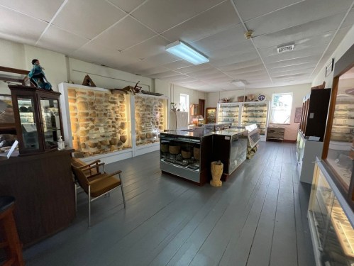 Interior of a museum displaying various artifacts in glass cases, with wooden furniture and a bright, open layout.