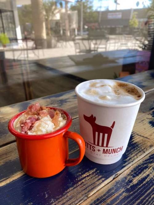 A small orange cup with a dessert topped with bacon bits next to a white coffee cup with a logo on a wooden table.