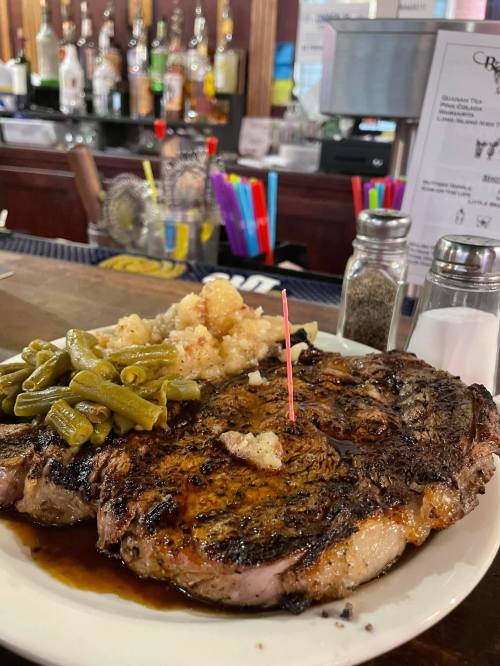 A plate of grilled steak with green beans and mashed potatoes, garnished with a toothpick, on a bar counter.