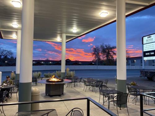 Outdoor seating area with a fire pit, surrounded by tables, under a colorful sunset sky.