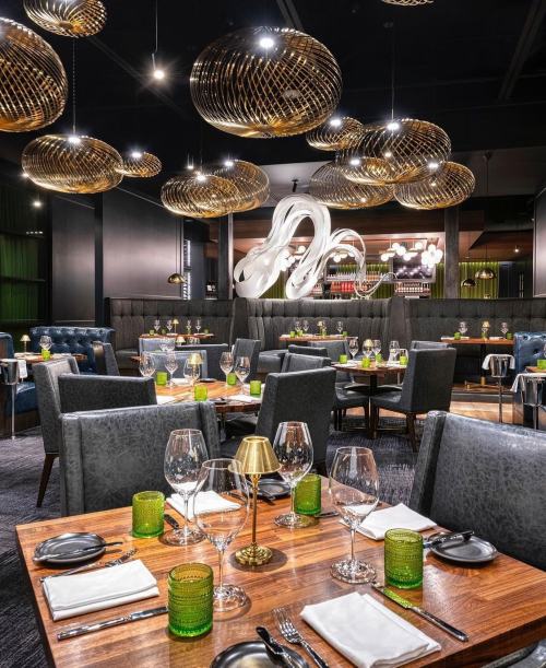 Elegant restaurant interior with modern decor, stylish lighting, and neatly set tables featuring green glassware.