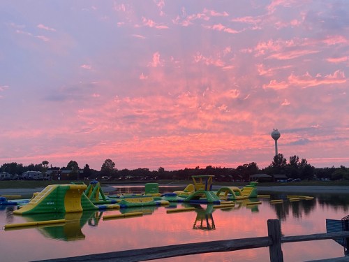Colorful inflatable water park on a lake at sunset, with vibrant clouds reflecting in the water.