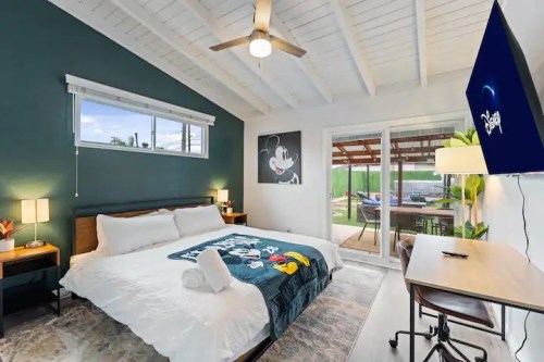 Cozy bedroom with a Mickey Mouse blanket, large windows, and a desk, featuring a modern design and outdoor view.