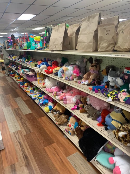 A colorful shelf filled with various stuffed animals and toys, with bags labeled "Toy" on the top shelf.