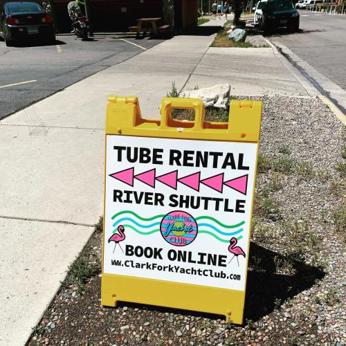 Sign for tube rental and river shuttle services, featuring colorful arrows and contact information for booking online.