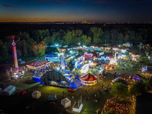 Aerial view of a vibrant carnival at dusk, featuring rides, food stalls, and crowds enjoying the festivities.