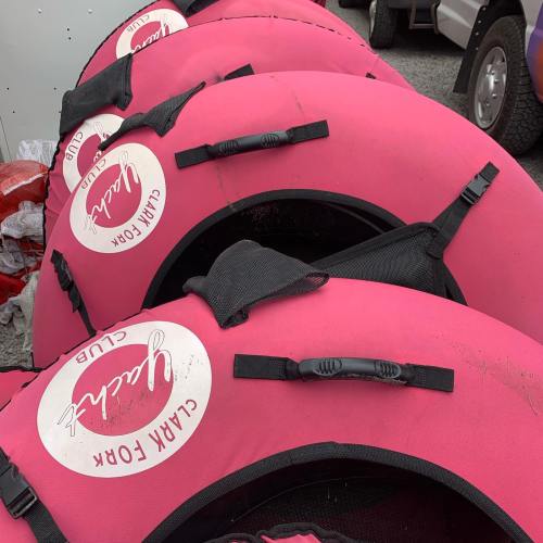A stack of pink inflatable tubes with white logos, resting on a gravel surface.