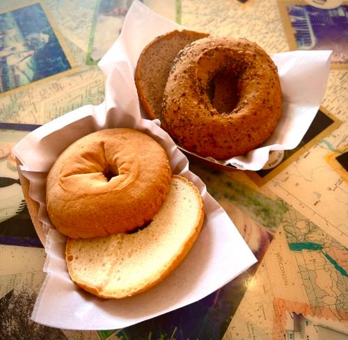Two bagels on a table, one plain and one with a poppy seed topping, served in paper baskets.