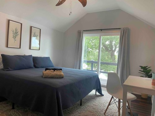 Cozy bedroom with a large bed, desk, and sliding glass door leading to a balcony, surrounded by greenery.