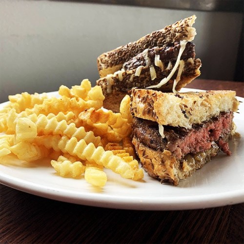 A plate with a sliced sandwich filled with meat and cheese, accompanied by a side of crinkle-cut fries.