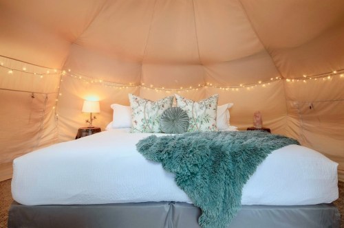 Cozy tent interior with a plush bed, decorative pillows, a soft blanket, and warm string lights.
