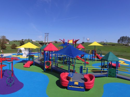 Colorful playground with various structures, slides, and climbing areas, set against a clear blue sky.