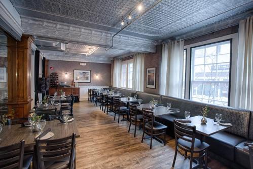 A cozy restaurant interior with wooden floors, tables set for dining, and large windows letting in natural light.