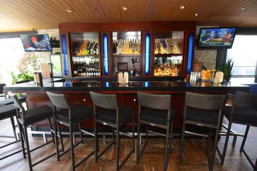 A modern bar with high stools, illuminated shelves of liquor, and a TV displaying sports in a stylish setting.