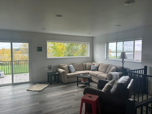 Bright living room with a beige couch, coffee table, and large windows overlooking greenery and a lake.
