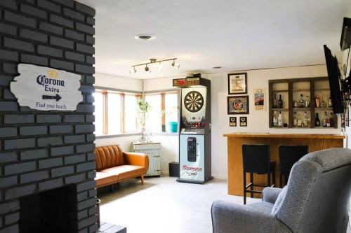 Cozy room featuring a bar, dartboard, seating area, and a Corona sign on the wall. Bright and inviting atmosphere.